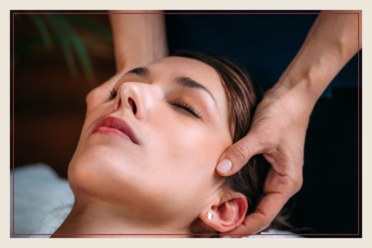 Both hands cradling a client's head as she rests face up on a towel, eyes closed