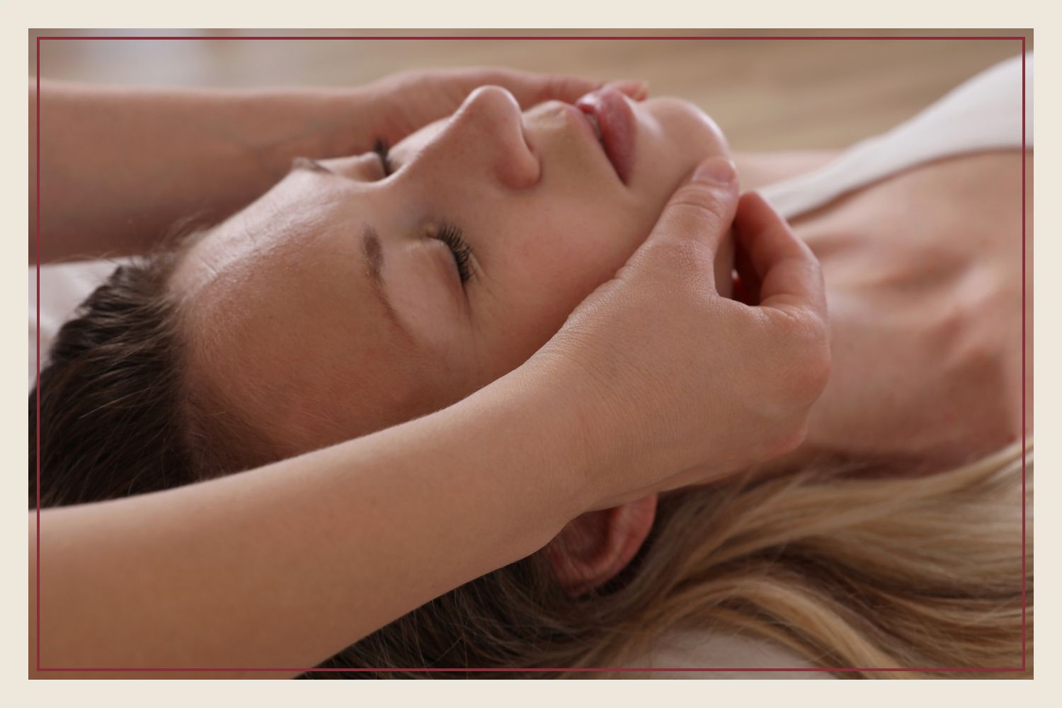 Hands gently cradling the face of a client lying face up with her eyes closed